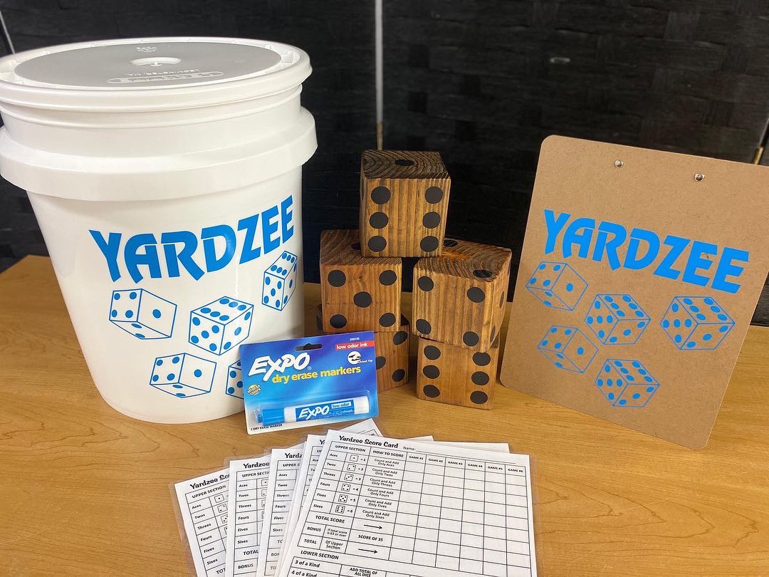 Yardzee game components including dice, bucket, and score sheets on a table.
