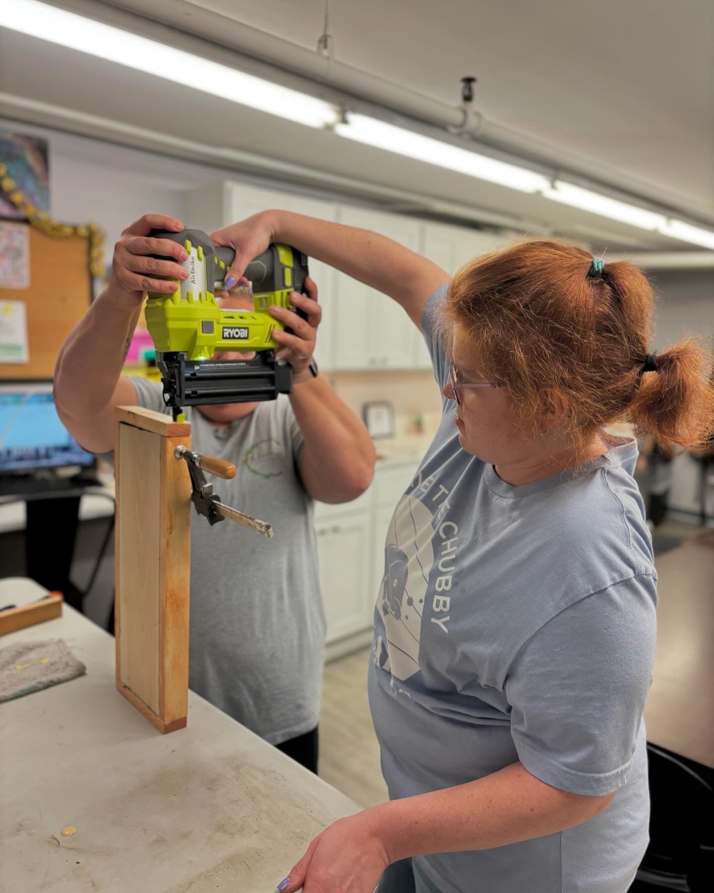 Two people working with a nail gun on a wooden project in a workshop.