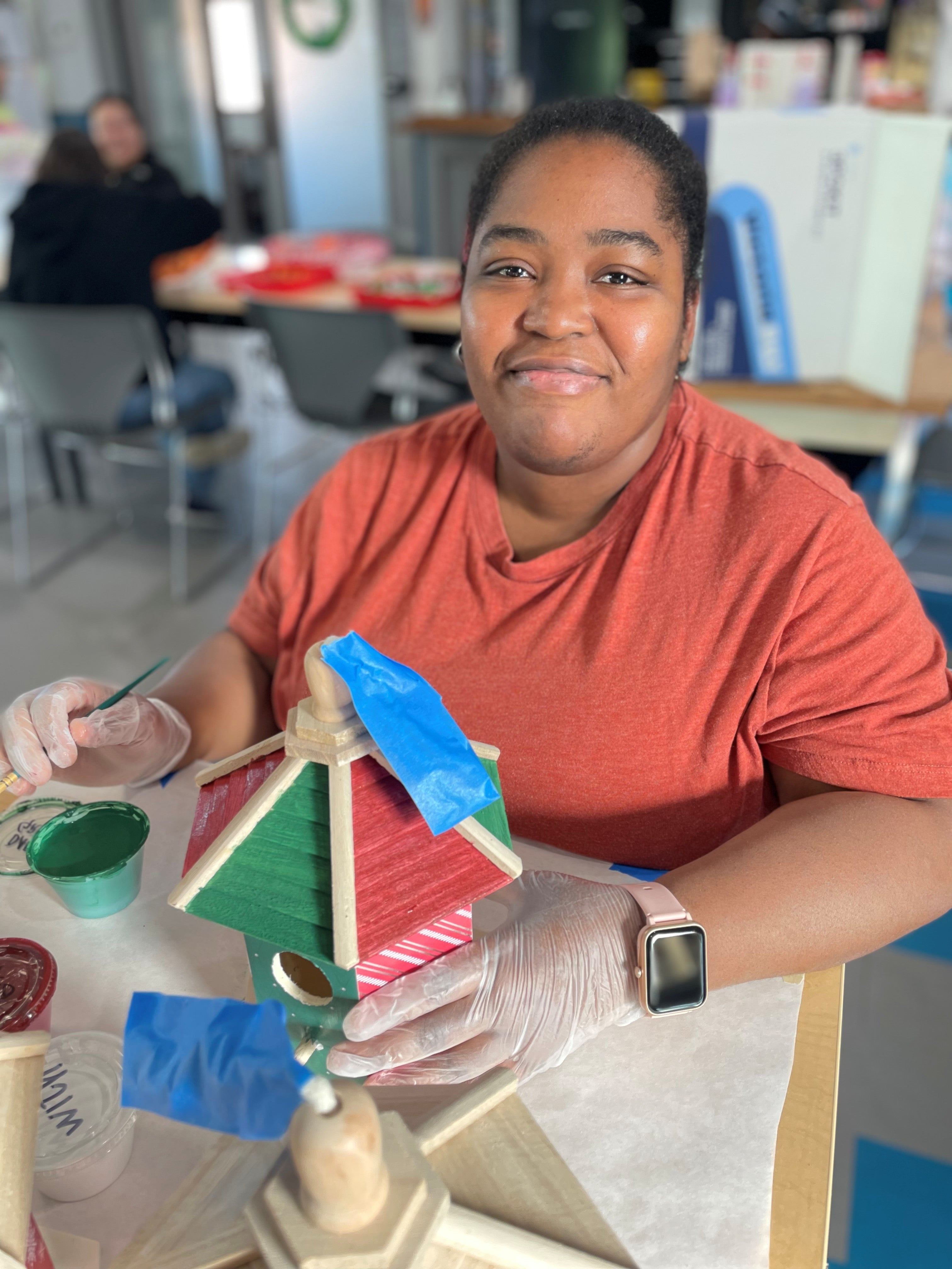 Young woman smiling, painting a red and green birdhouse