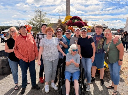 Group of people posing outdoors with a person in a wheelchair, under a blue sky with clouds.