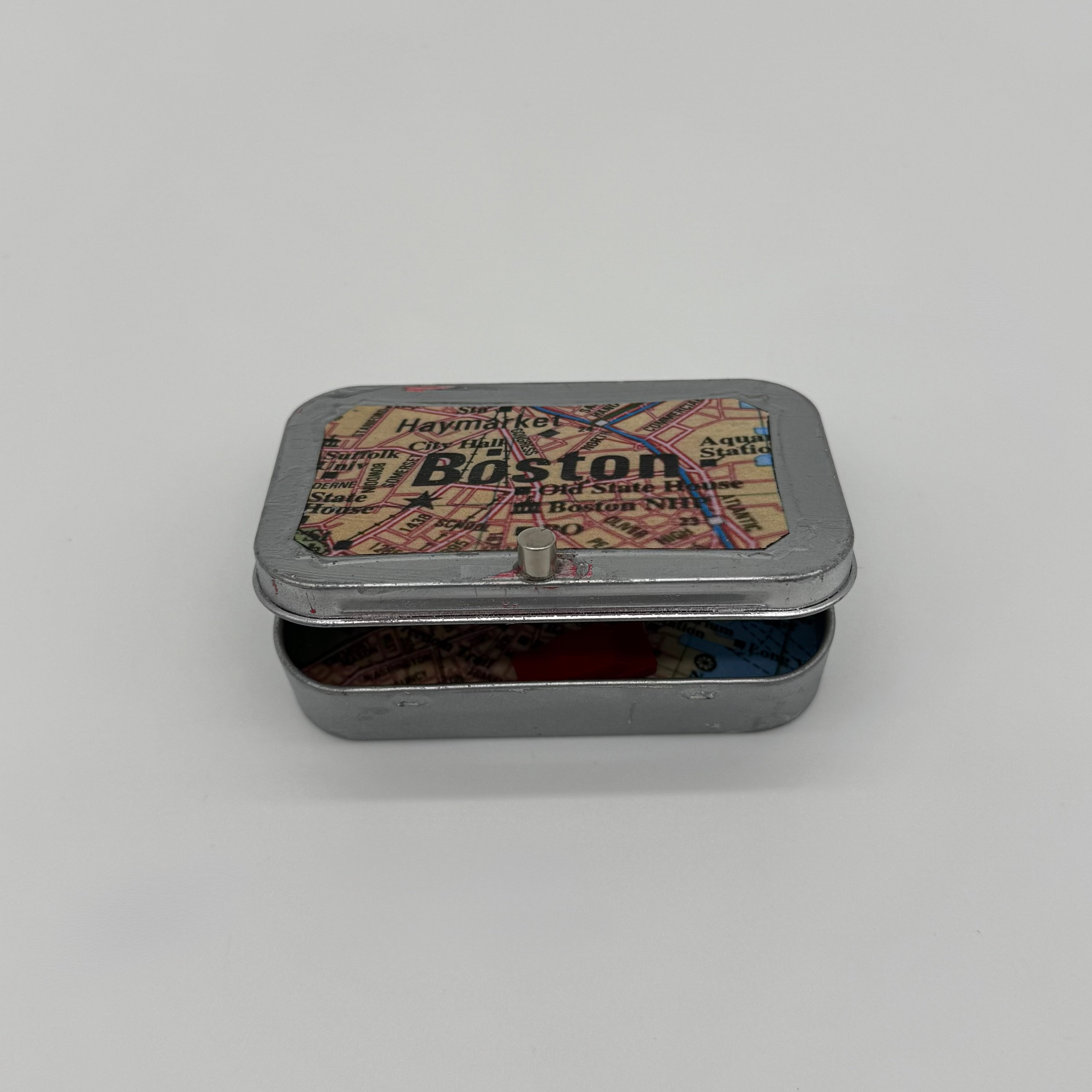 Small metal box with a decorative lid featuring "Boston" text and map graphics on a light gray background