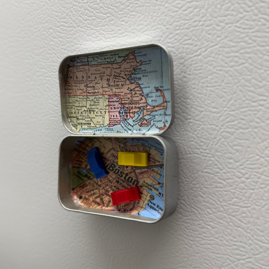Small metal tin with a map design containing colorful cars on a white fridge
