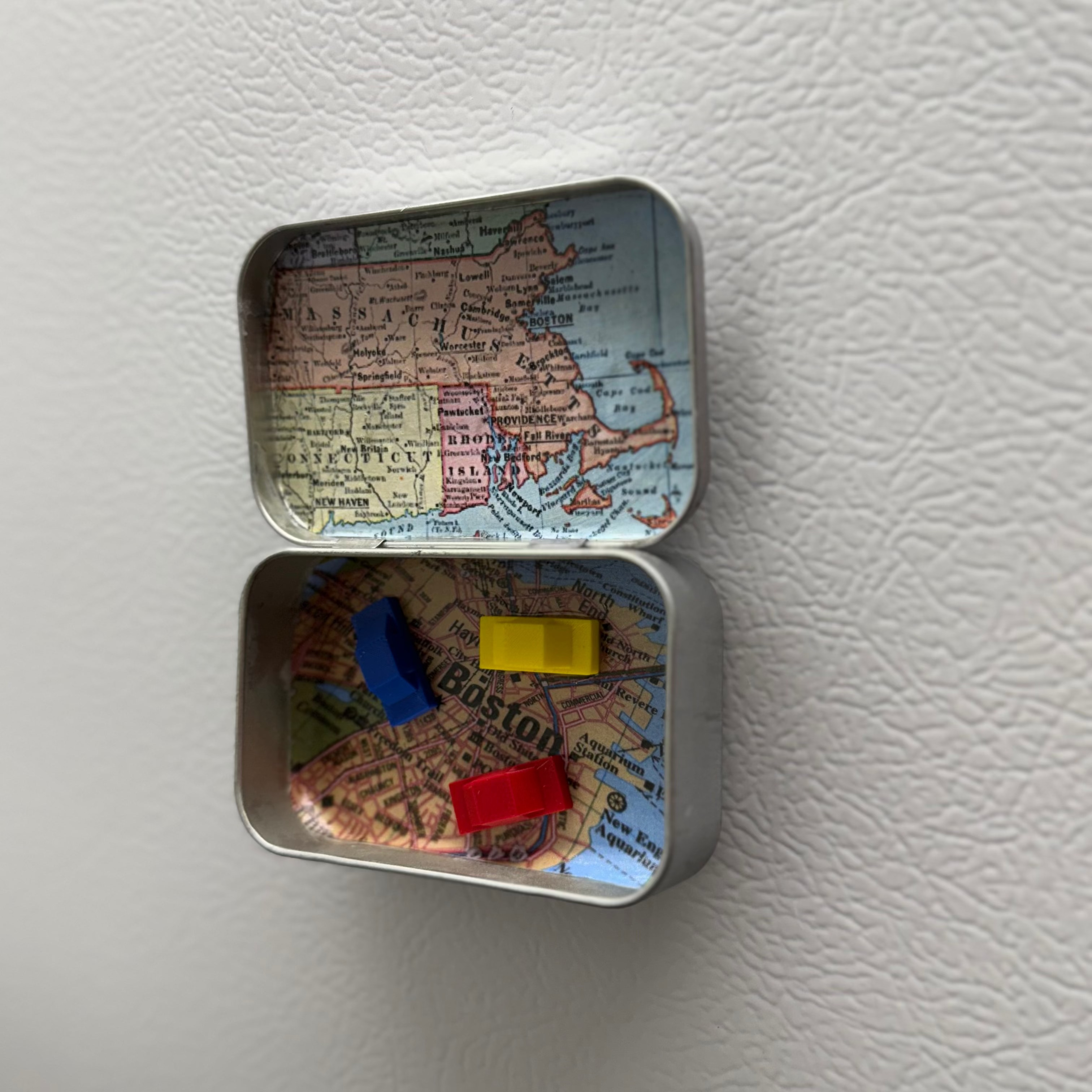 Small metal tin with a map design containing colorful cars on a white fridge