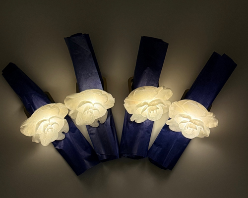 Four white glowing floral napkin rings on a dark background