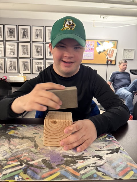 Young man smiling, sanding a wooden block