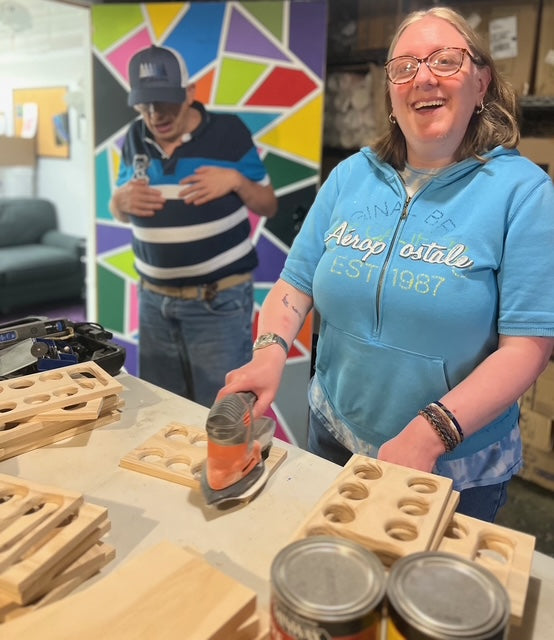 Person sanding a wooden block with cans on a table, colorful wall in the background