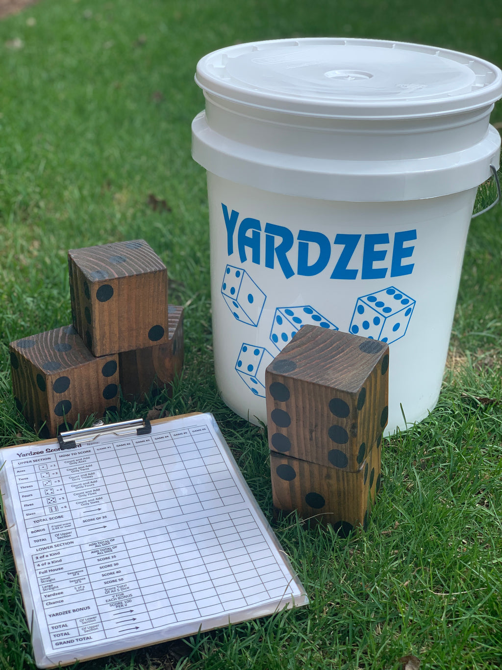Yardzee game set with wooden dice, a score sheet, and a white bucket on grass.