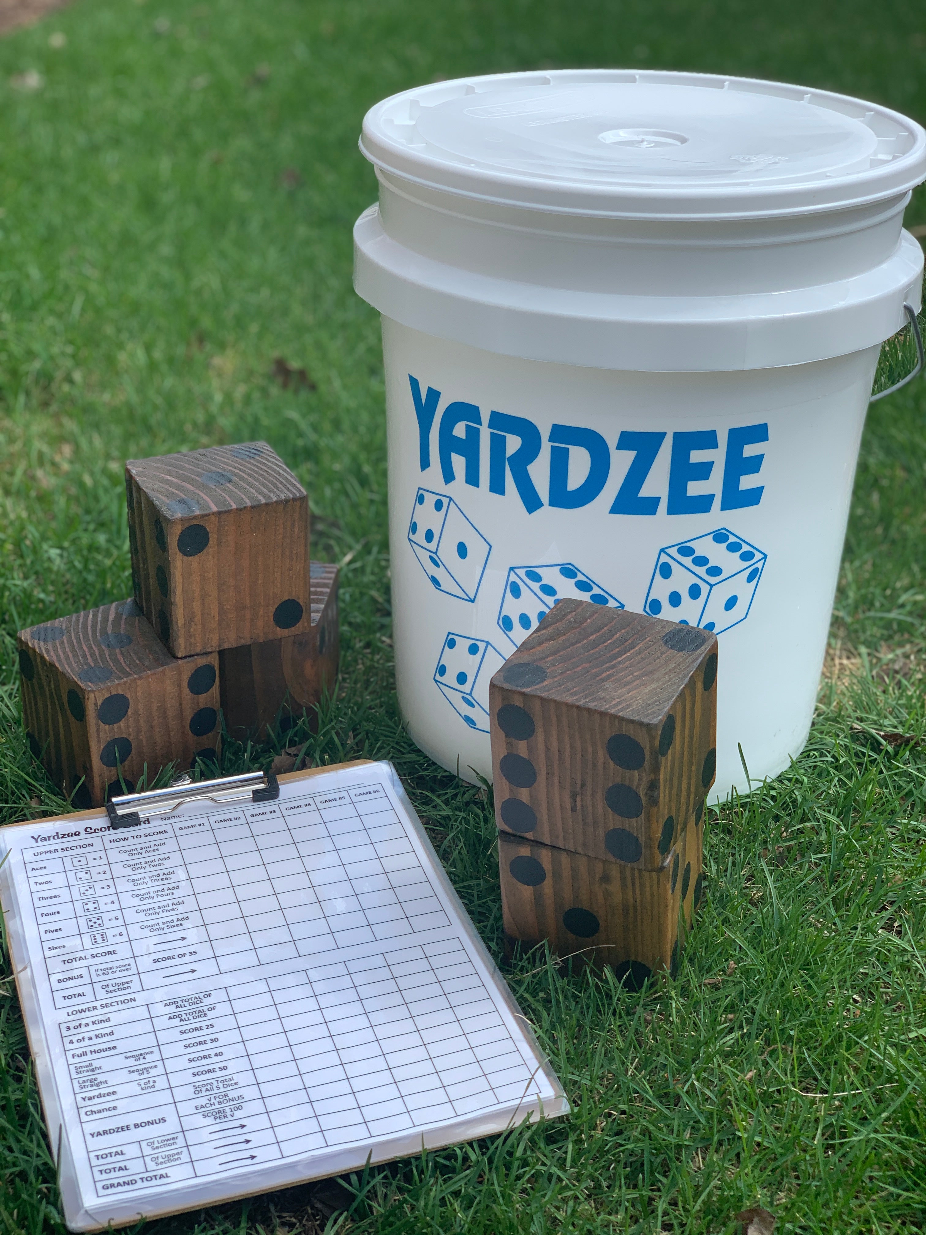 Yardzee game set with wooden dice, a score sheet, and a white bucket on grass.