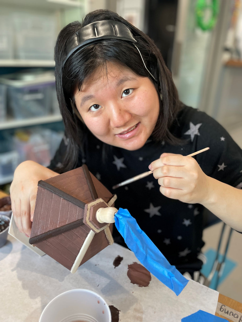 Young woman smiling, painting a brown birdhouse