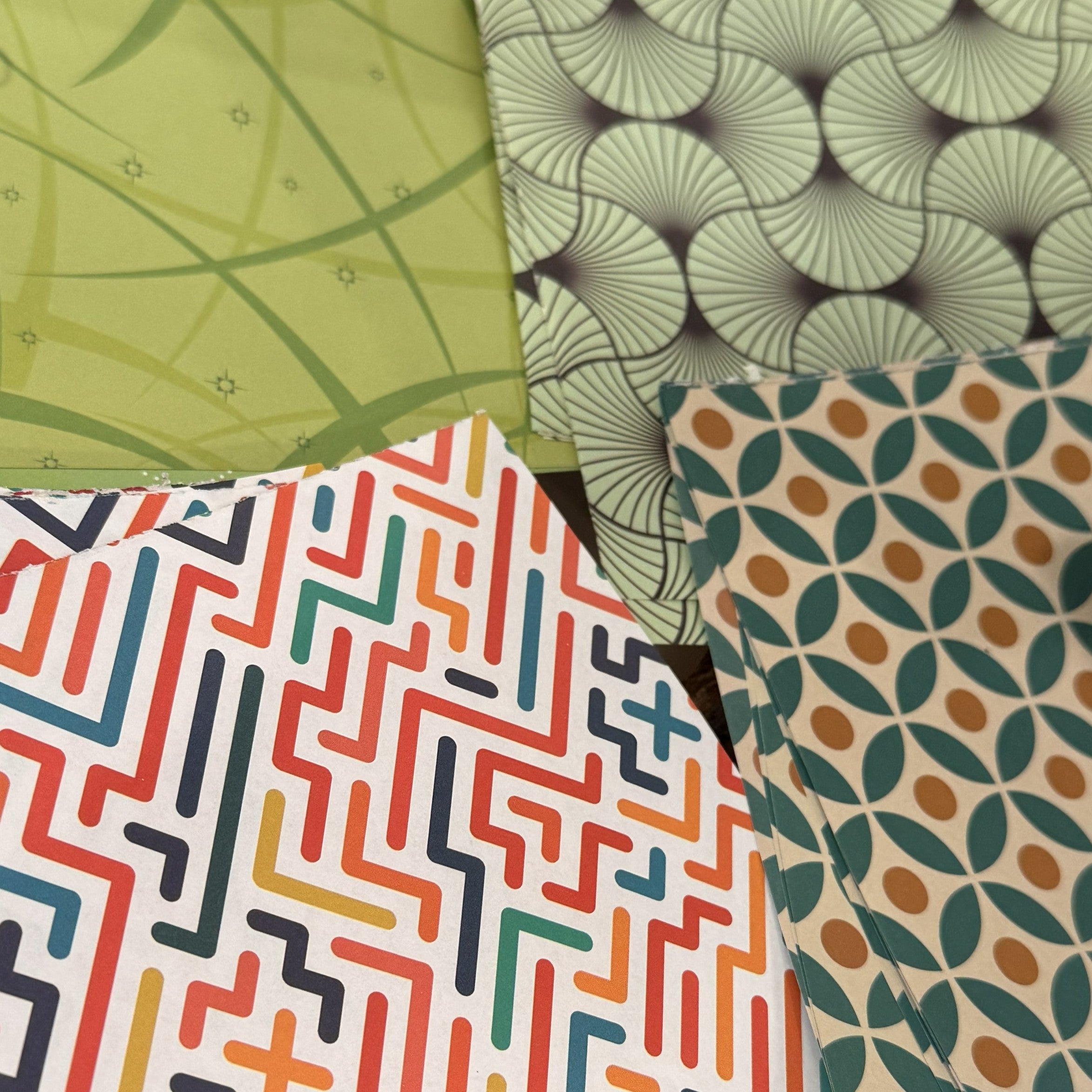 Four overlapping patterned fabric or paper swatches with geometric and floral designs in green, gray, white, red, orange, blue, and beige.