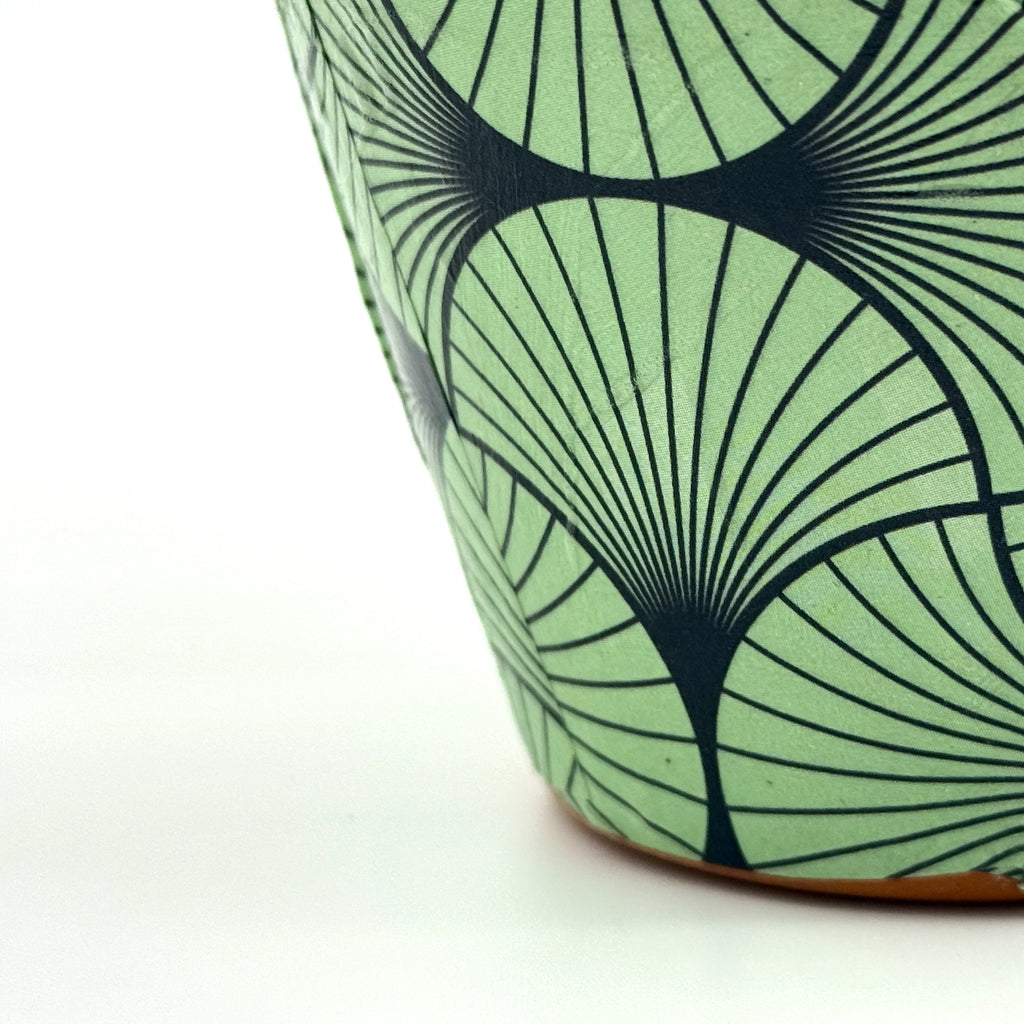 Close-up of a ceramic planter with a mint green and black geometric fan pattern, shown on a white background.