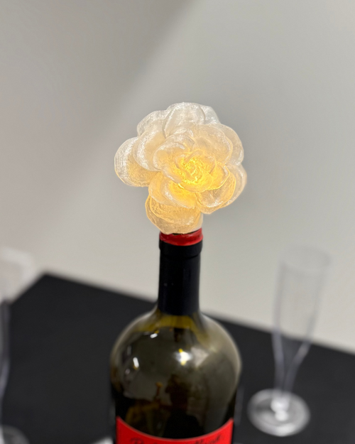 Wine bottle with decorative flower on top on a black surface with glasses in the background