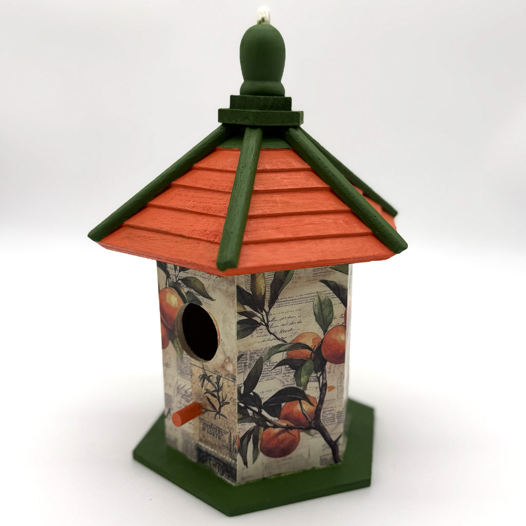 Decorative birdhouse with an orange roof and fruit design on a white background